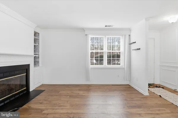 a view of an empty room with wooden floor fireplace and a window