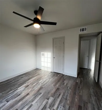 a view of an empty room with wooden floor and a ceiling fan