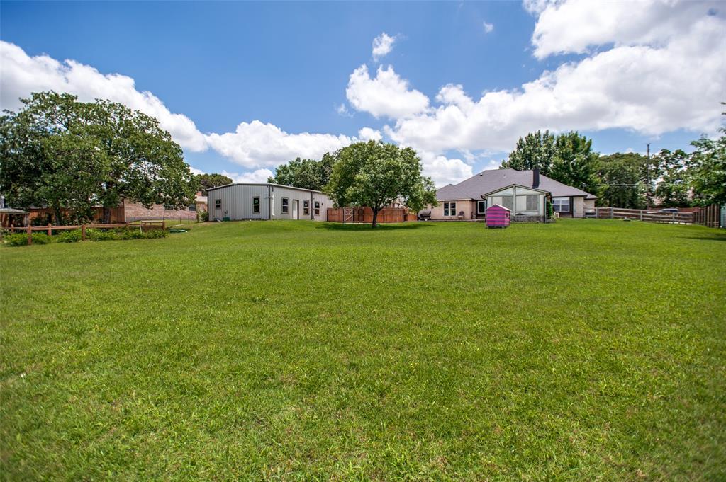 5643 West Caylor Road Fort Worth, TX 76244 - Photo 33 of 37 Expansive rear yard featuring a detached auxiliary building, mature trees, wood fencing, and a primary residence with a sunroom addition