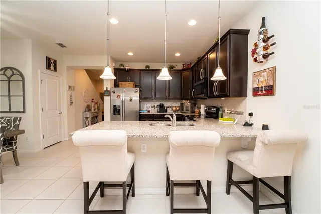 a kitchen with stainless steel appliances kitchen island granite countertop a refrigerator a stove a sink and a dining table with white cabinets