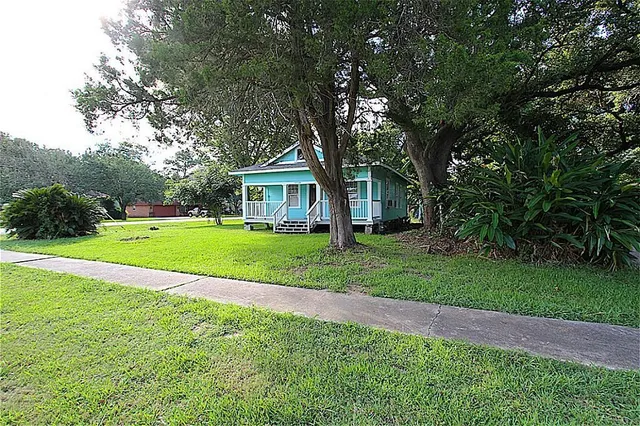 a view of house in front of a big yard with large trees
