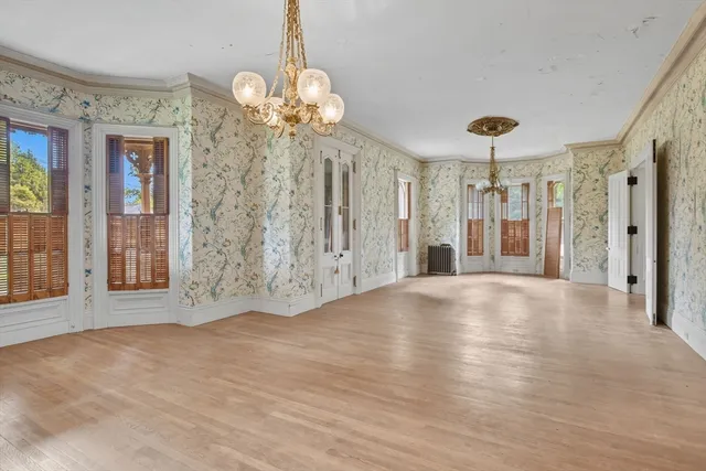 a view of an empty room with chandelier and wooden floor