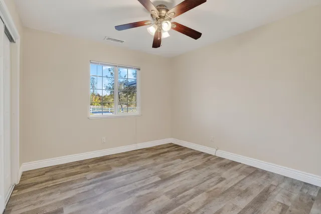 an empty room with wooden floor ceiling fan and window