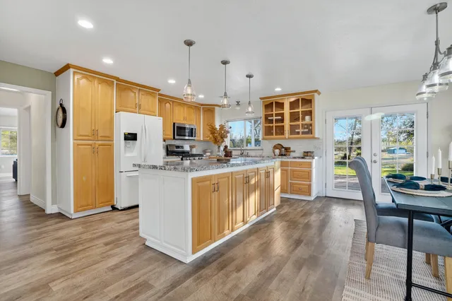 a kitchen with stainless steel appliances granite countertop a refrigerator a stove top oven a sink dishwasher and white cabinets with wooden floor