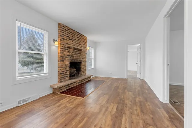 a view of an empty room with wooden floor fireplace and a window