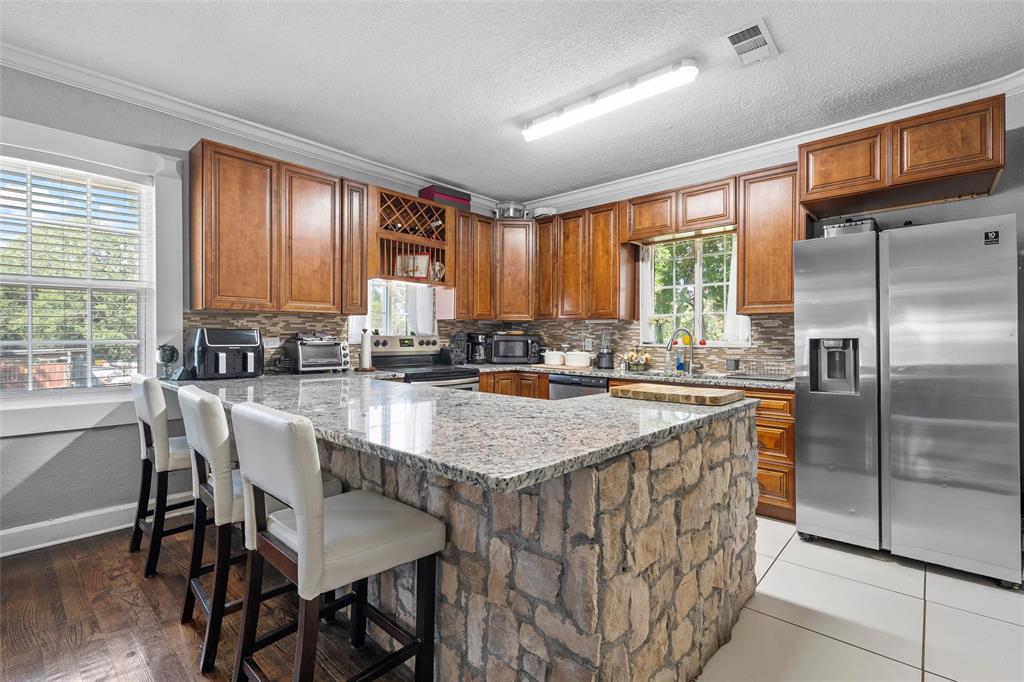 2700 Cole Avenue Waco, TX 76707 - Photo 7 of 14 Kitchen with stainless steel appliances, a peninsula, light stone countertops, brown cabinetry, and ornamental molding