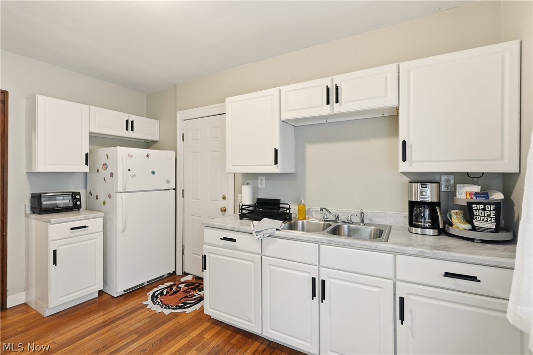 3579 Bosworth Road Cleveland, OH 44111 - Photo 15 of 39 Kitchen featuring white cabinetry with black hardware, a dual-basin stainless steel sink, light-toned countertops, and wood-finish flooring