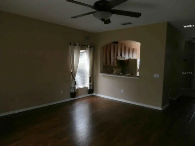 a view of empty room with wooden floor and fan