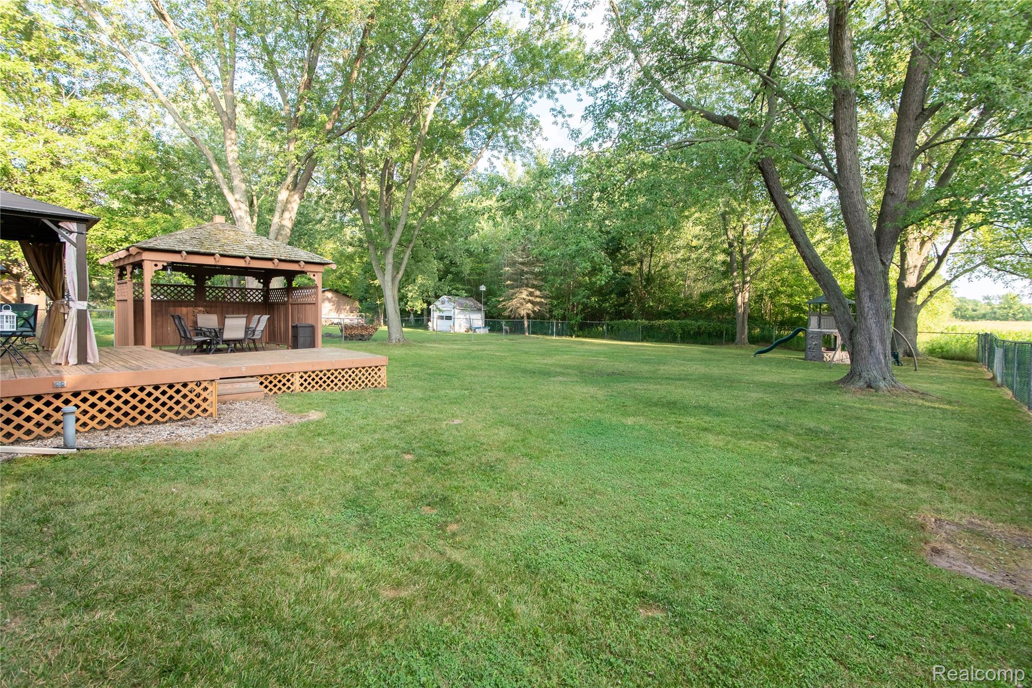 4395 Regency Road Swartz Creek, MI 48473 - Photo 61 of 67 Expansive green lawn featuring a built-in wooden deck with lattice skirting, a screened gazebo, and mature trees