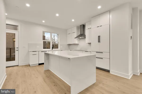 a large kitchen with kitchen island a sink a stove a refrigerator and white cabinets with wooden floor