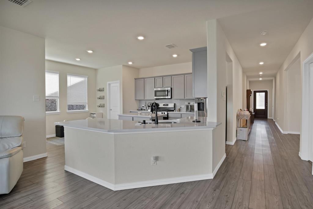 621 Ridgeback Trail Fort Worth, TX 76052 - Photo 3 of 22 Open-concept kitchen featuring an island with a light-toned countertop, gray cabinetry, stainless steel appliances, and recessed lighting