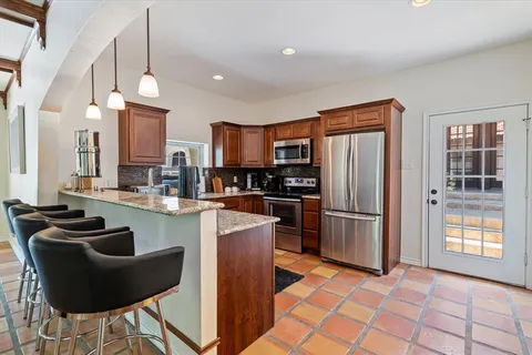 a kitchen with stainless steel appliances granite countertop a refrigerator a sink a stove a dining table and chairs