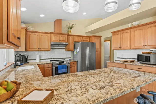 a kitchen with stainless steel appliances granite countertop wooden cabinets a stove a sink and a dining table with wooden floor