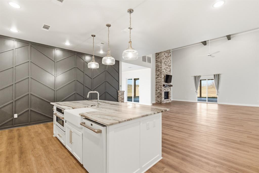 4600 A Old Brock Road Weatherford, TX 76087 - Photo 9 of 40 Two tone kitchen featuring an accent wall, a kitchen island with sink, two tone cabinets, decorative light fixtures, and light wood-type flooring