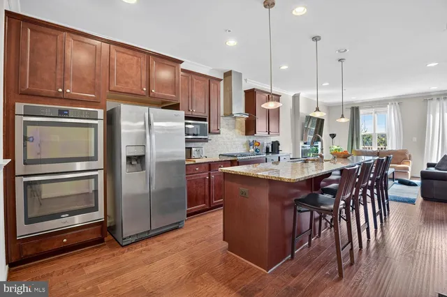 a kitchen with stainless steel appliances granite countertop a refrigerator a stove a sink a dining table and chairs with wooden floor