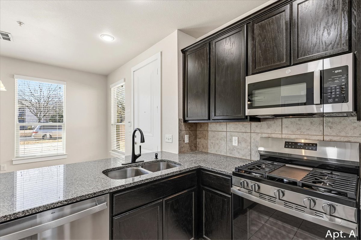 2225 Katy Lane, Unit A Georgetown, TX 78626 - Photo 11 of 22 Kitchen with stainless steel appliances, light stone countertops, decorative backsplash, tile patterned floors, and dark cabinetry
