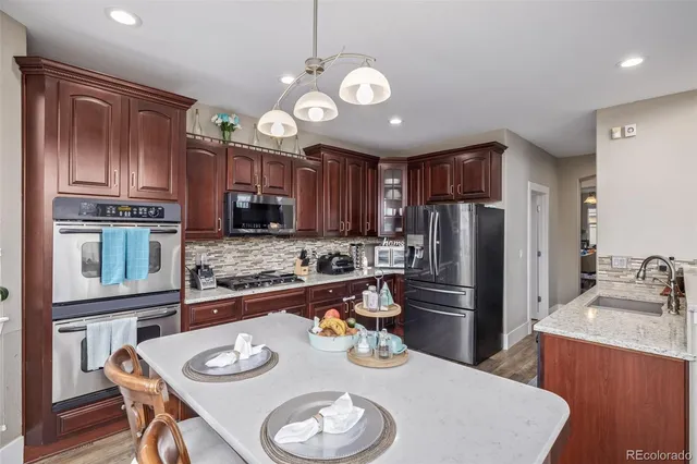 a kitchen with granite countertop stainless steel appliances a sink a stove a refrigerator cabinets and dining table