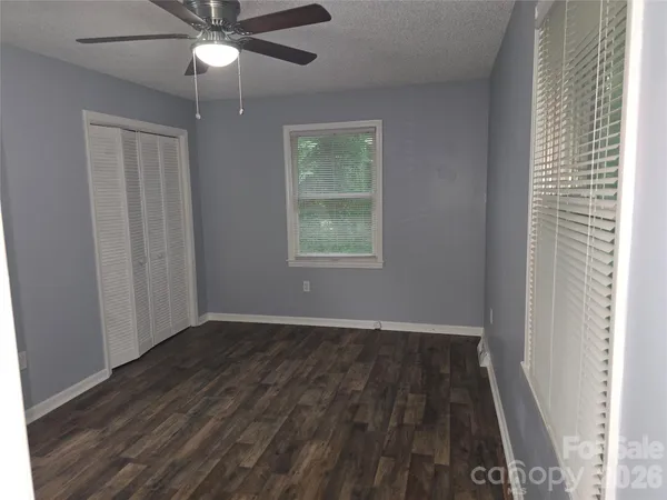 an empty room with wooden floor fan and windows