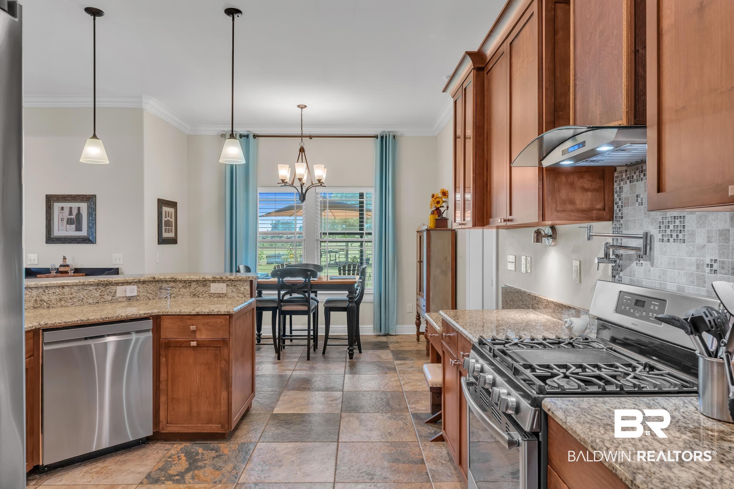 28918 Comstock Road Elberta, AL 36530 - Photo 29 of 53 Kitchen featuring stainless steel appliances, brown cabinetry, crown molding, a chandelier, and backsplash