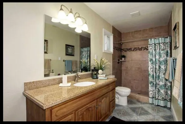 a bathroom with a granite countertop sink a toilet a mirror a vanity and shower