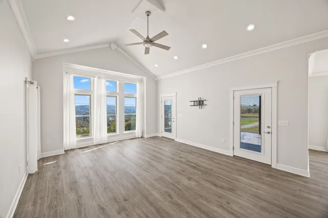 a view of an empty room with wooden floor ceiling fan and window