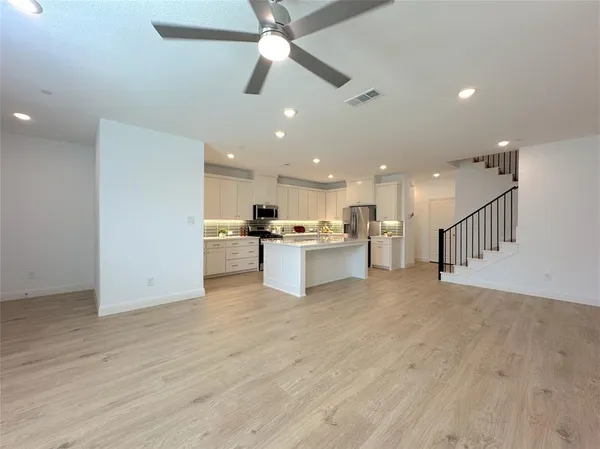 a view of kitchen with kitchen island stainless steel appliances wooden floor cabinets oven and a sink