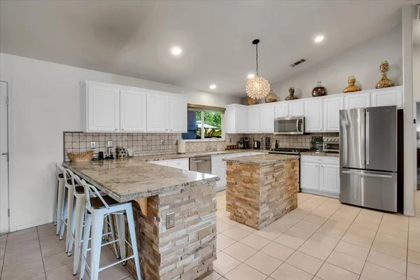 a kitchen with kitchen island granite countertop a stove a refrigerator a oven a white table and chairs with white cabinets