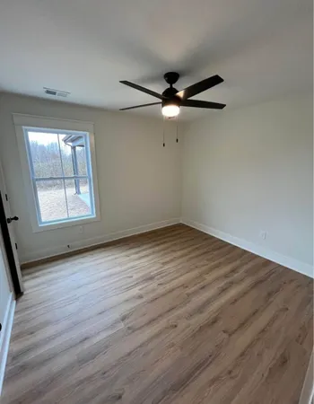 an empty room with wooden floor fan and windows
