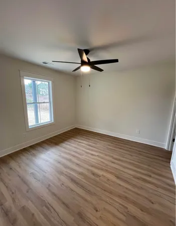 an empty room with wooden floor fan and windows