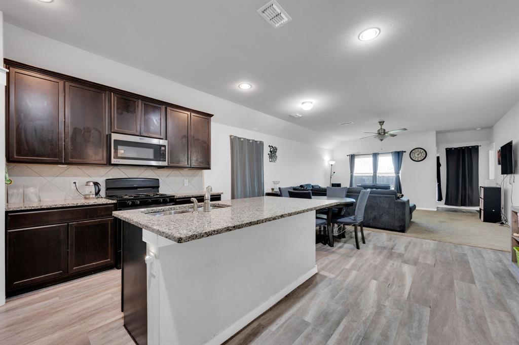 2609 Centurion Road Glenn Heights, TX 75154 - Photo 29 of 29 Kitchen featuring light stone counters, dark wood finish cabinets, open floor plan, an island with sink, and recessed lighting