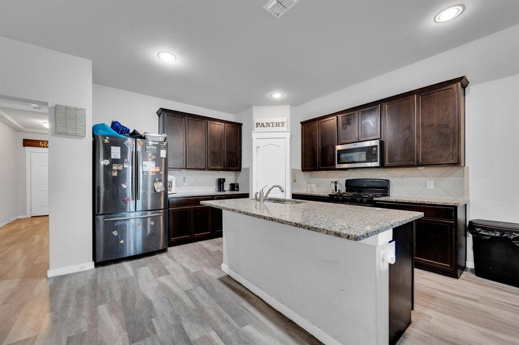 2609 Centurion Road Glenn Heights, TX 75154 - Photo 7 of 29 Kitchen with stainless steel appliances, dark wood finish cabinets, an island with sink, light stone countertops, and backsplash