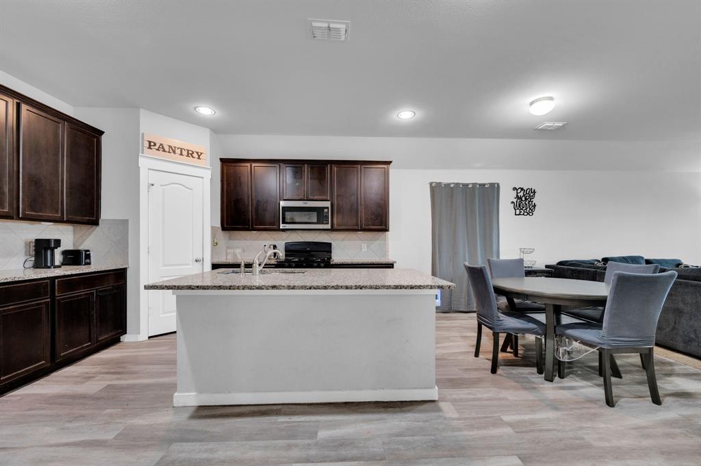 2609 Centurion Road Glenn Heights, TX 75154 - Photo 9 of 29 Kitchen featuring dark wood finish cabinets, light stone counters, a center island with sink, stainless steel microwave, and gas stove