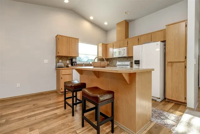 a kitchen with stainless steel appliances granite countertop a refrigerator a sink a stove a dining table and chairs with wooden floor