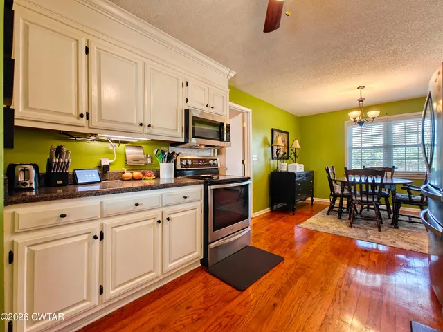 a kitchen with stainless steel appliances granite countertop a stove top oven a sink a dining table and chairs with wooden floor