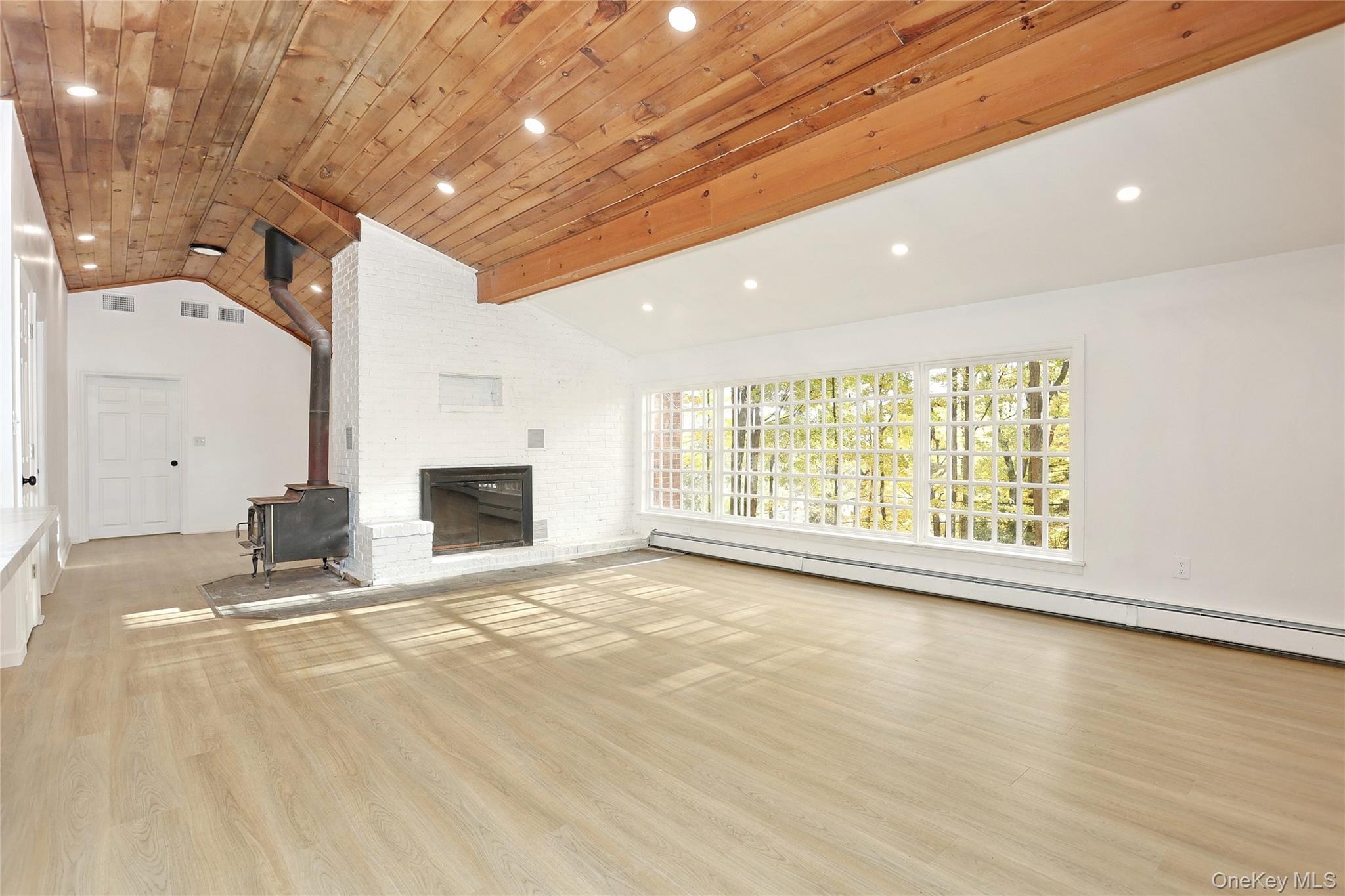 84 Pine Hill Road Chester, NY 10918 - Photo 12 of 18 Unfurnished living room featuring a wood stove, beamed ceiling, light wood-style flooring, baseboard heating, and high vaulted ceiling