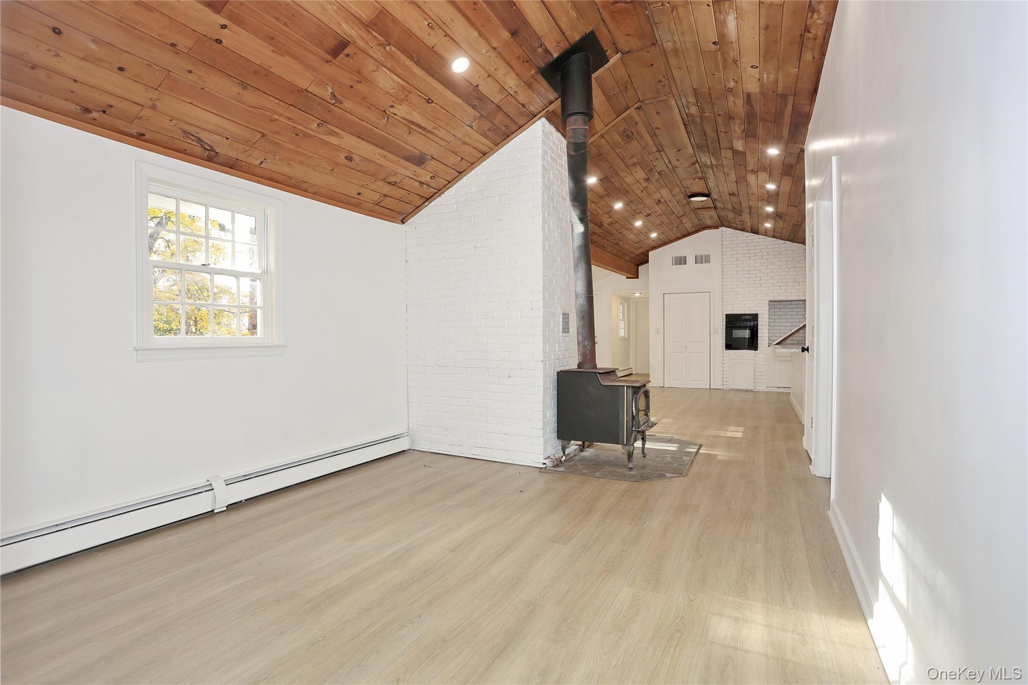 84 Pine Hill Road Chester, NY 10918 - Photo 13 of 18 Unfurnished living room featuring a wood stove, a baseboard heating unit, light wood-type flooring, recessed lighting, and wood ceiling