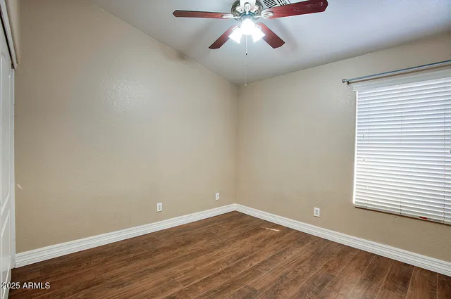 an empty room with wooden floor chandelier fan and windows