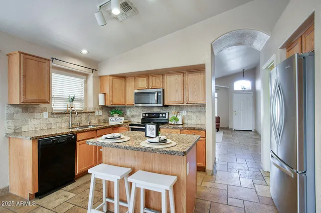 a kitchen with stainless steel appliances granite countertop a sink a stove a refrigerator cabinets and chairs