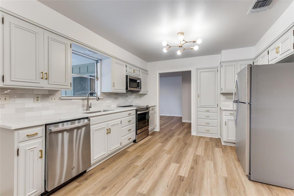 a kitchen with granite countertop a refrigerator oven a sink dishwasher and white cabinets with wooden floor