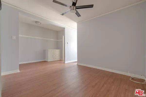 a view of an empty room with wooden floor and a ceiling fan