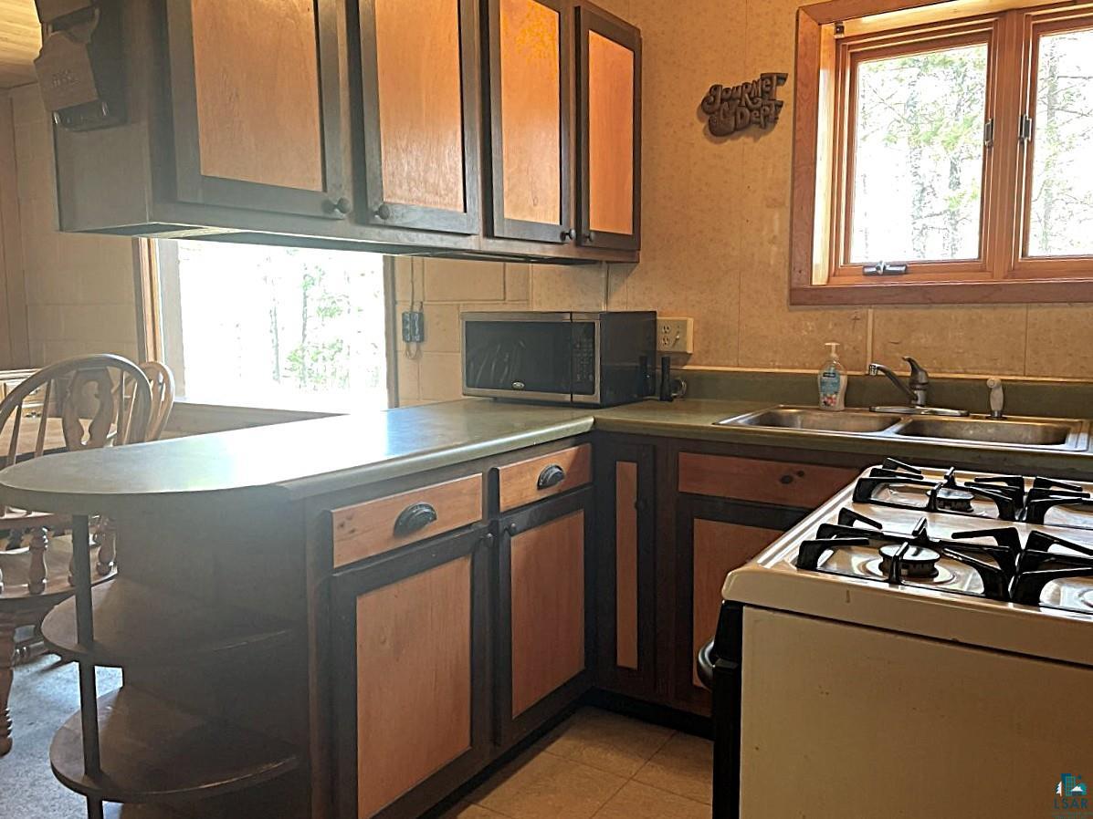 1480 Maijala Road Ely, MN 55731 - Photo 17 of 58 Kitchen featuring wood cabinetry with dark frames, a built-in breakfast bar, a double basin stainless steel sink, and gas stove.