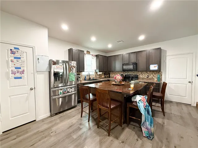 a kitchen with granite countertop a refrigerator a stove a sink a dining table and chairs