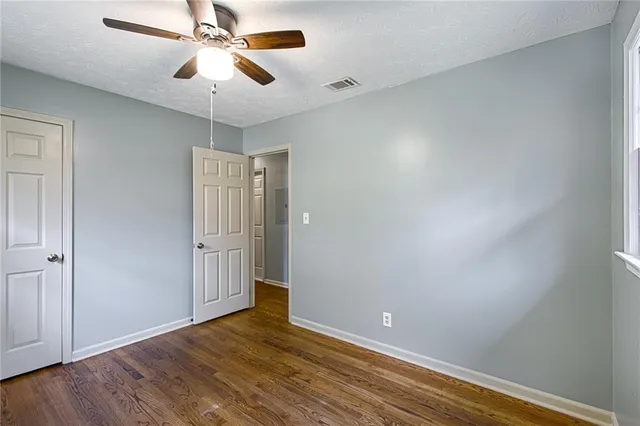 an empty room with wooden floor fan and windows