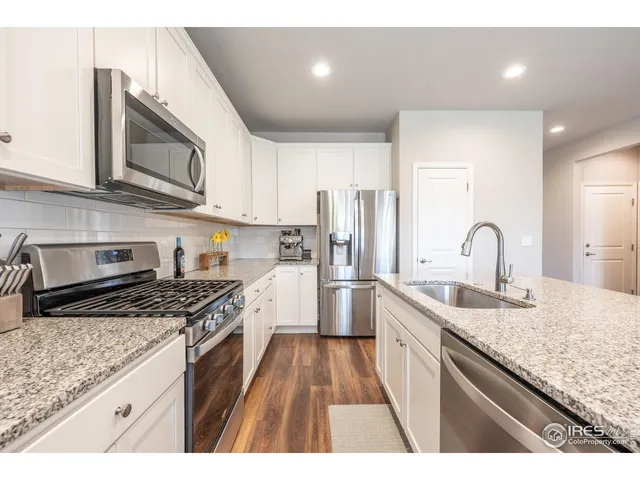 a open kitchen with stainless steel appliances granite countertop a refrigerator a stove a sink dishwasher a dining table and chairs with wooden floor