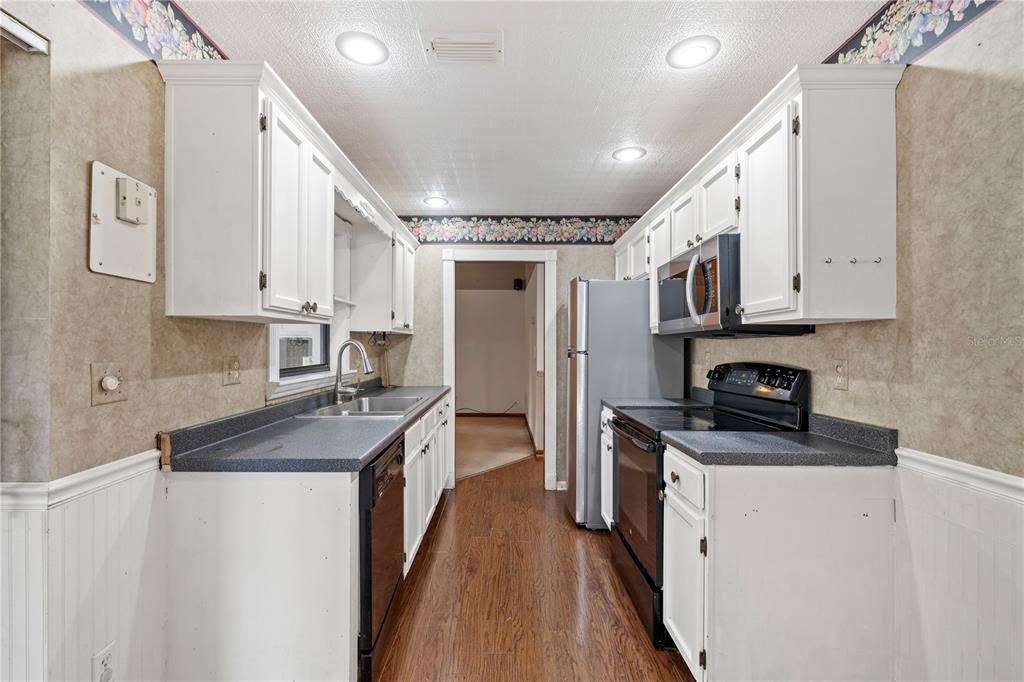 5444 Lighthouse Road Orlando, FL 32808 - Photo 18 of 36 a kitchen with stainless steel appliances granite countertop a stove top oven a sink a refrigerator white cabinets and wooden floor