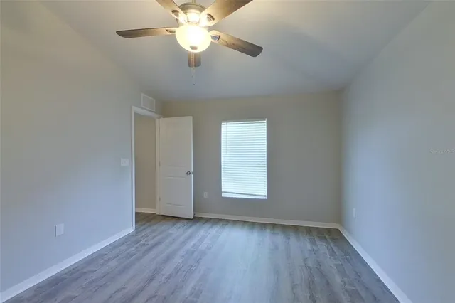 an empty room with wooden floor fan and windows