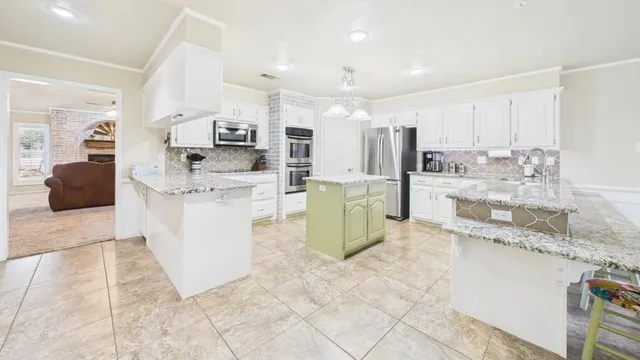 a large white kitchen with stainless steel appliances kitchen island granite countertop a sink and cabinets