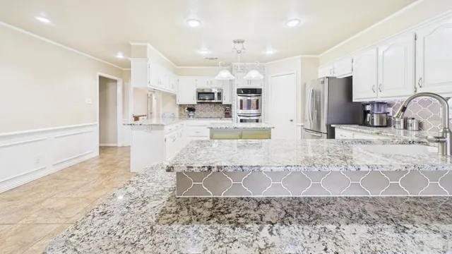 a large kitchen with kitchen island granite countertop a stove a sink a refrigerator white cabinets and couches