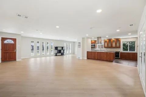a view of an empty room with kitchen and window