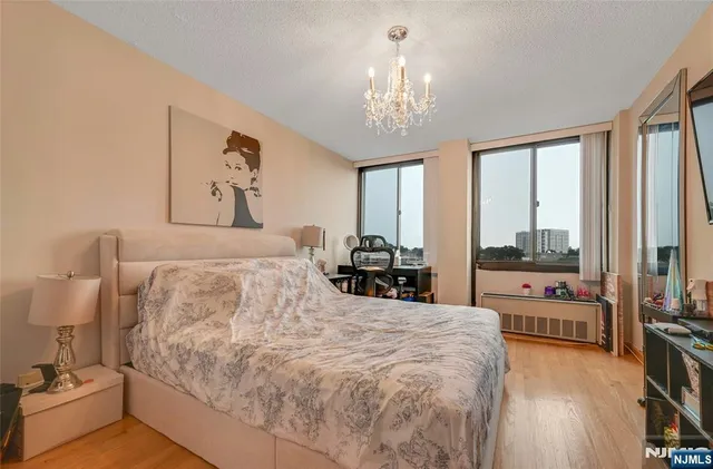 a bedroom with bed a chandelier and a flat tv screen on dresser